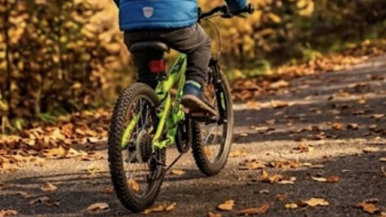 Kind mit Helm auf einem Fahrrad zwischen buntem Herbstlaub