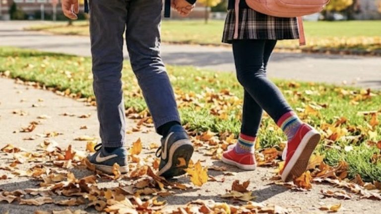 Schulkinder mit Rucksäcken auf einem Weg mit Herbstlaub